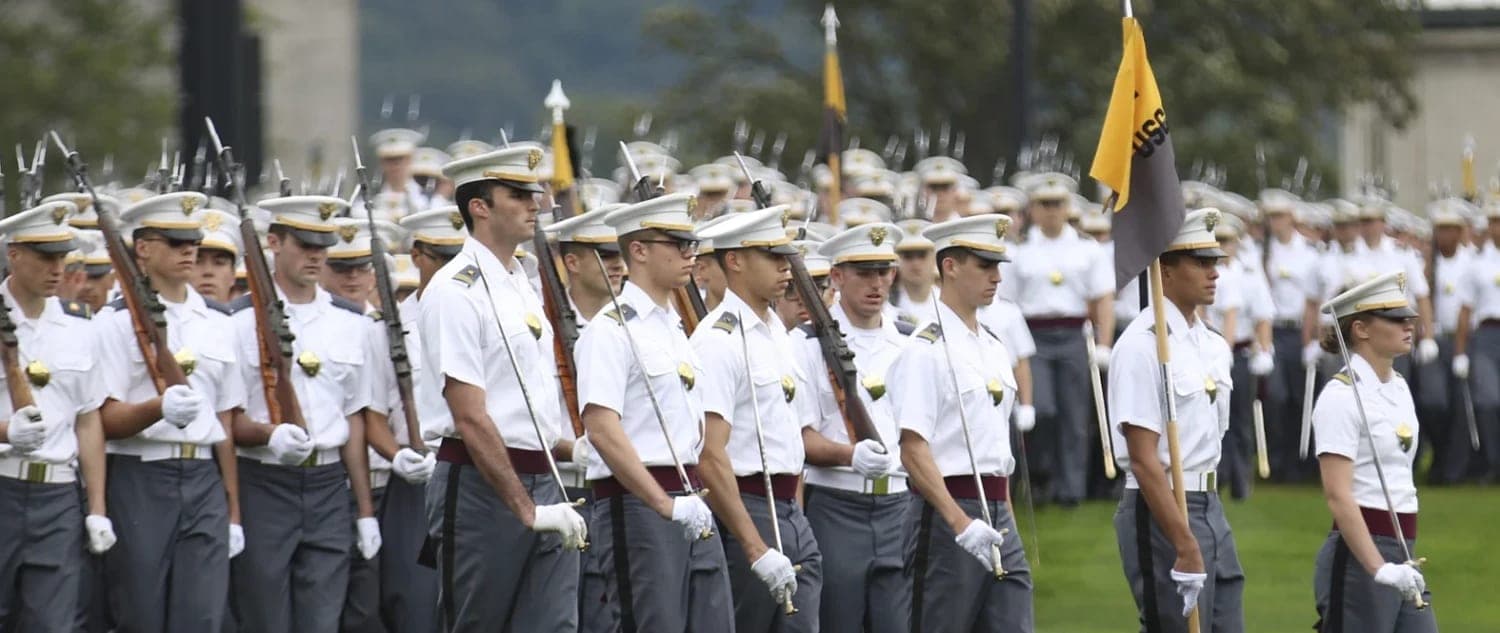 West Point cadets in full dress marching on parade, a gold company flag at the front